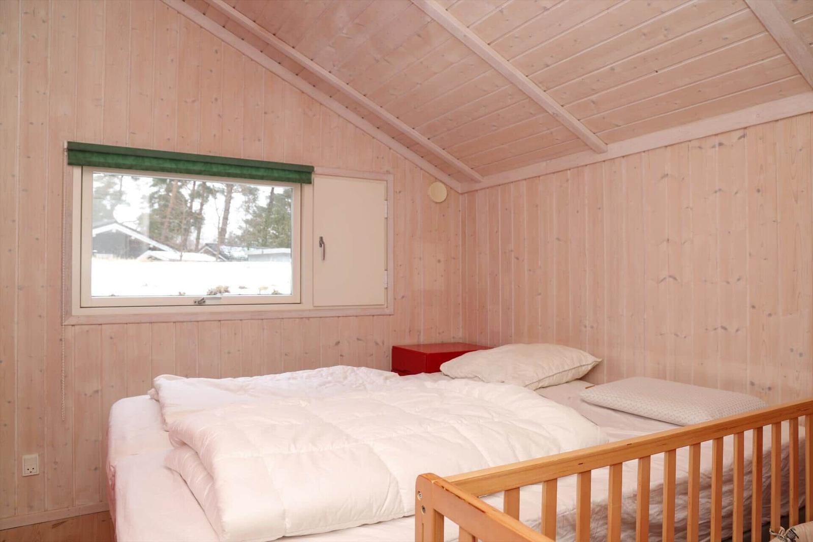 Schlafzimmer mit Holzwand, Fenster und Babybett.