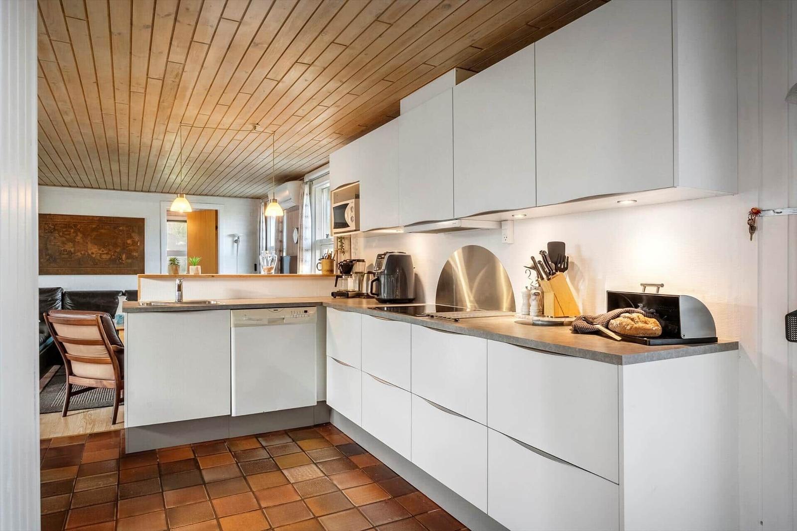 Küche mit weißen Schränken, Holzdecke und Terrakottboden. Auf der Arbeitsfläche steht ein Laib Brot.