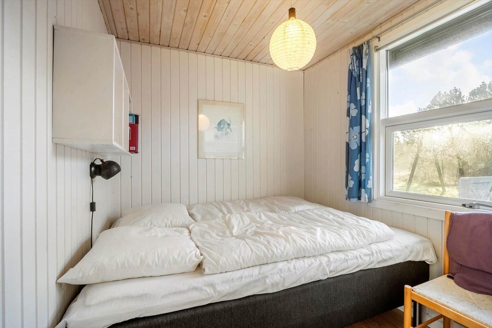 Schlafzimmer mit Bett, Fenster und Deckenleuchte.