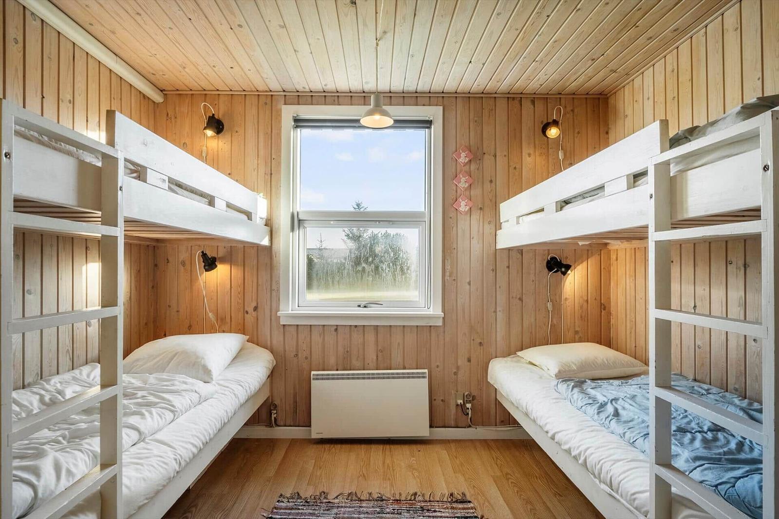 Zwei Stockbetten mit Matratzen und Kissen. Holzwände und Boden. Fenster mit Blick nach draußen.