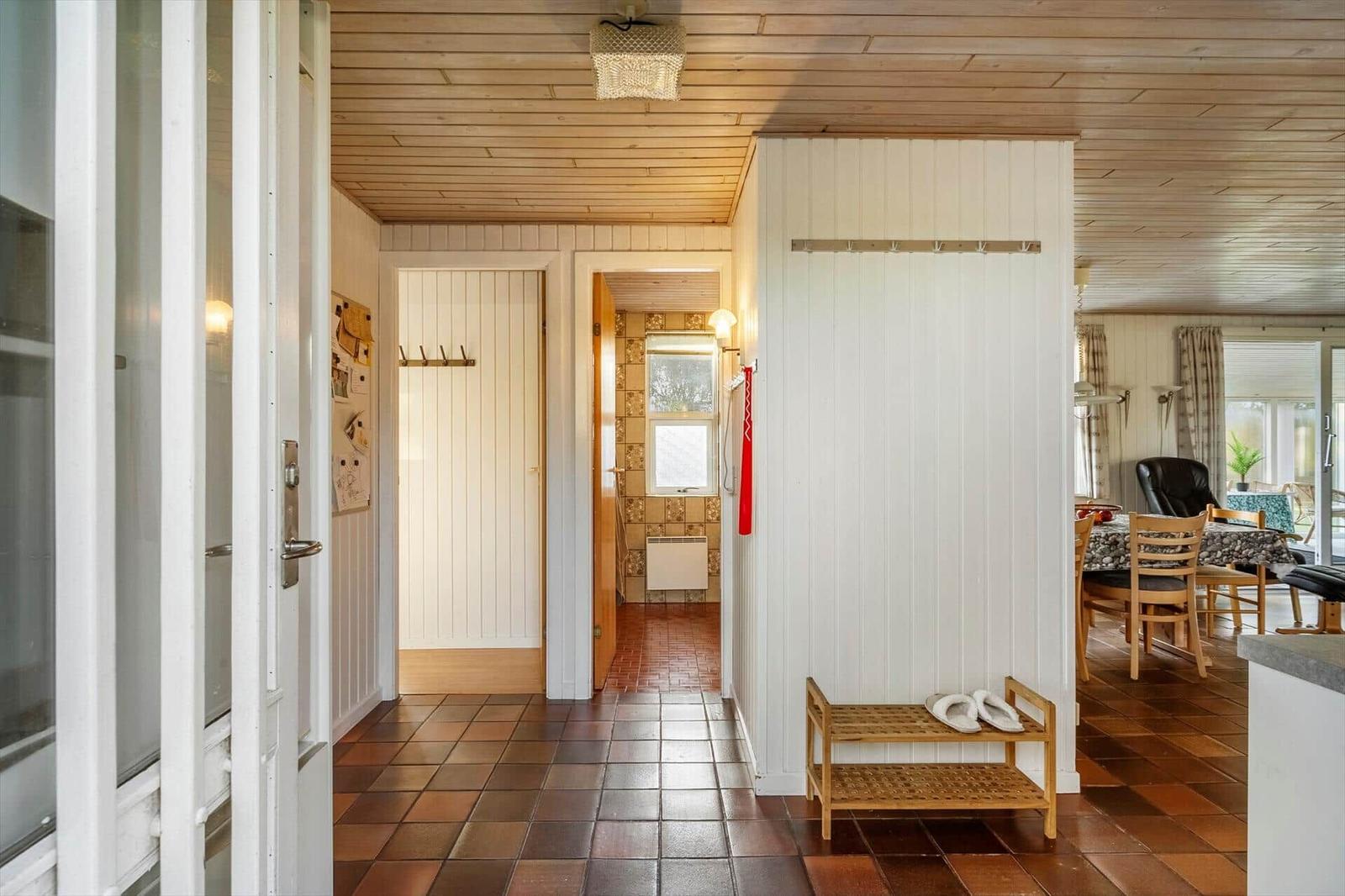 Hausflur mit Holzdecke, gefliestem Boden und Schuhbank. Tür führt ins Bad.