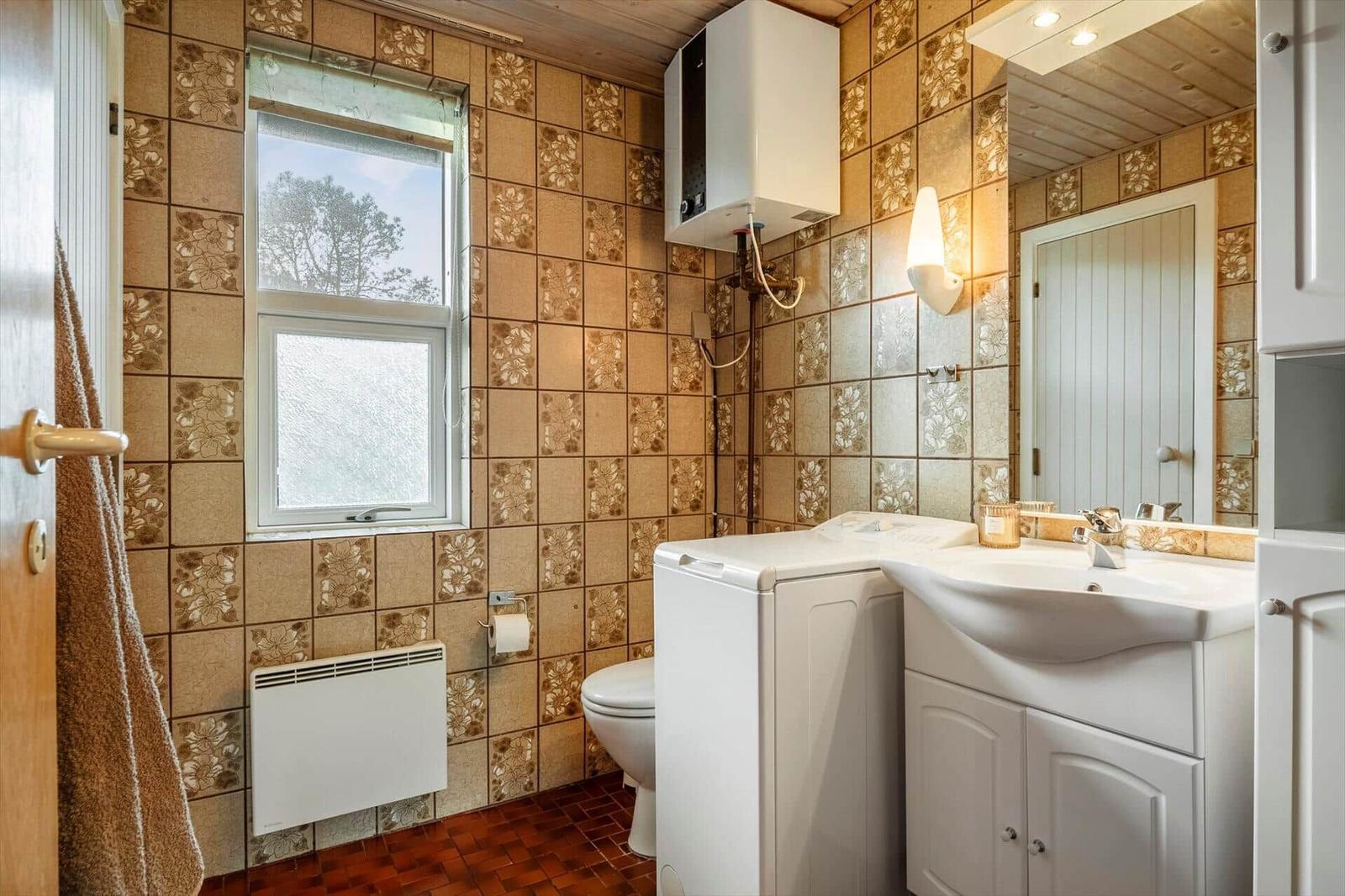 Badezimmer mit Waschmaschine, Toilette und Spiegel. Wandfliesen und Holzdecke.
