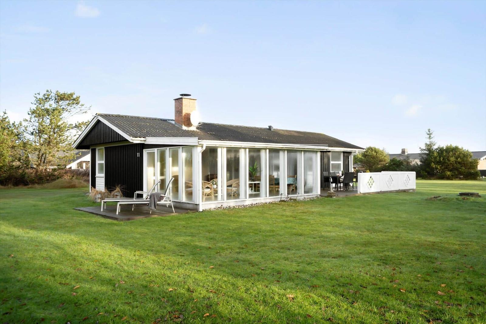Moderne Villa mit großem Garten und Terrasse. Glasfront zeigt Wohnbereich.