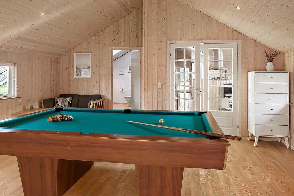 Room with pool table, sofa, and white cabinets. Wooden walls and ceiling.