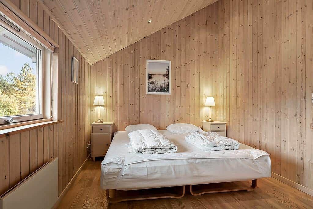 Bedroom with wood paneling, bed, and window with view of forest.