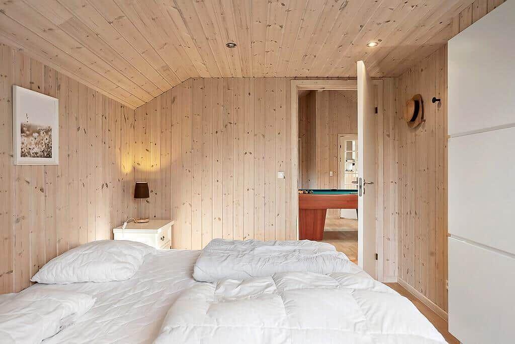 Bedroom with wooden walls and bed. Passage to room with billiard table.