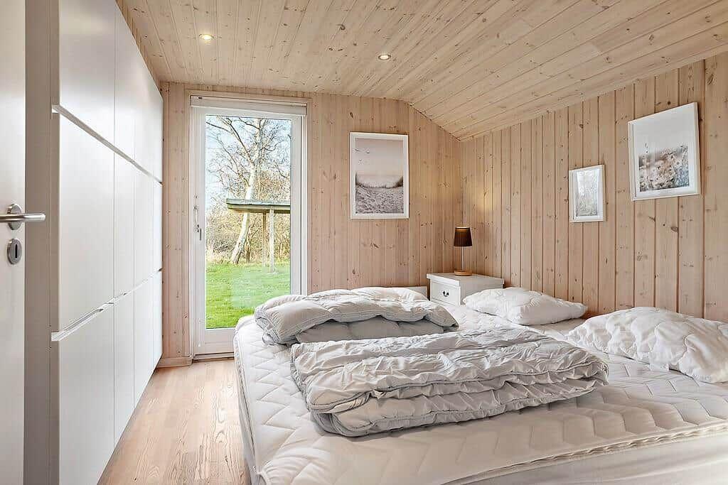 Bedroom with wooden walls, bed, and window overlooking greenery.