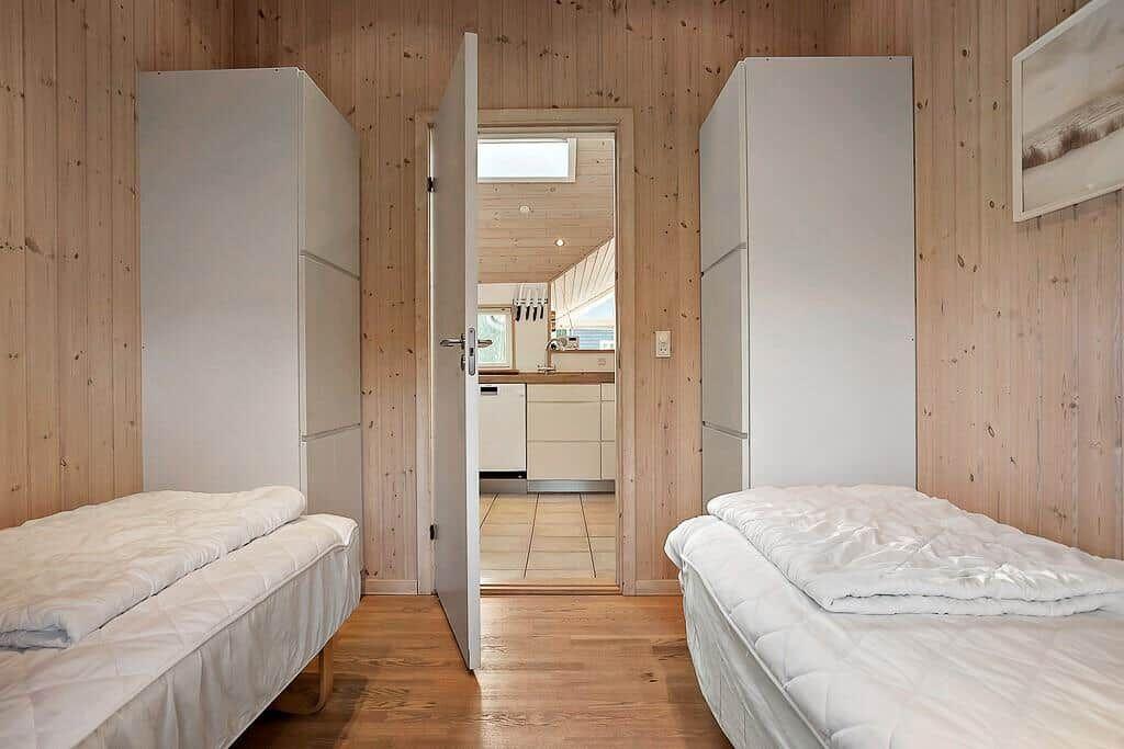 Two beds in a room with wood walls and door to kitchen.