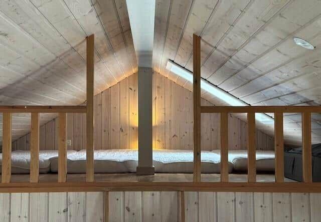Upper sleeping area with wooden railing and sloped ceiling.