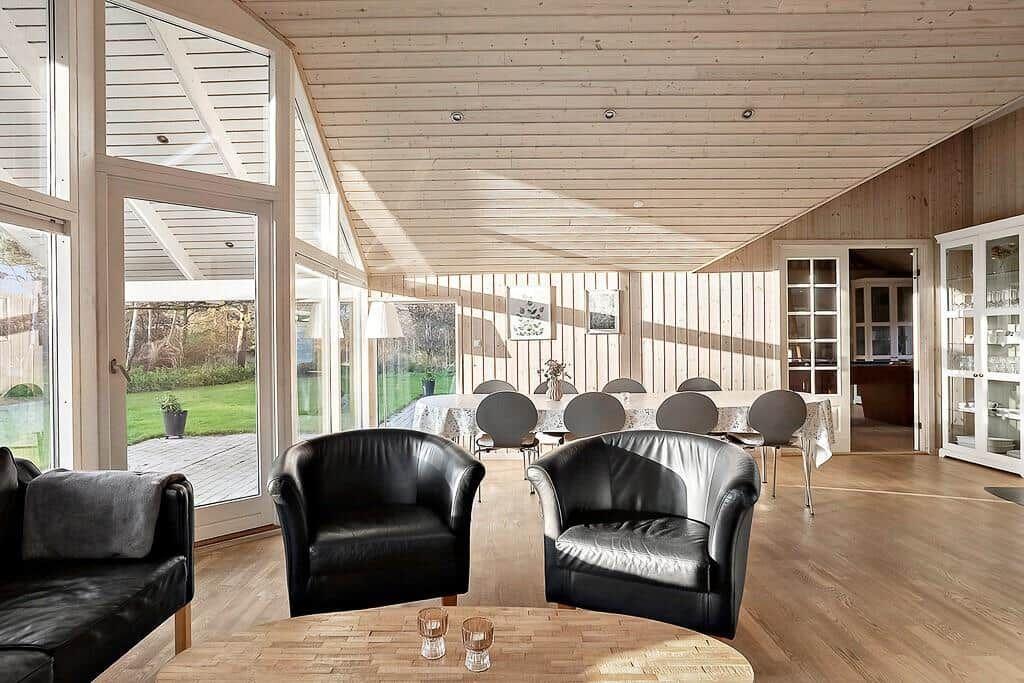 A room with wooden ceiling, black chairs, and large windows overlooking the garden.