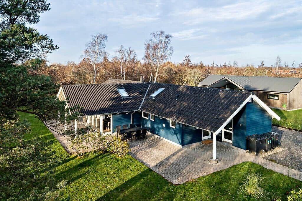 Blue house with terrace and garden. Roof with skylights. Surrounded by trees.