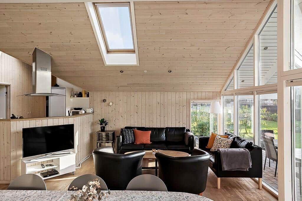 Living area with wooden walls, sofa, seating group, and TV. Large windows and skylight.