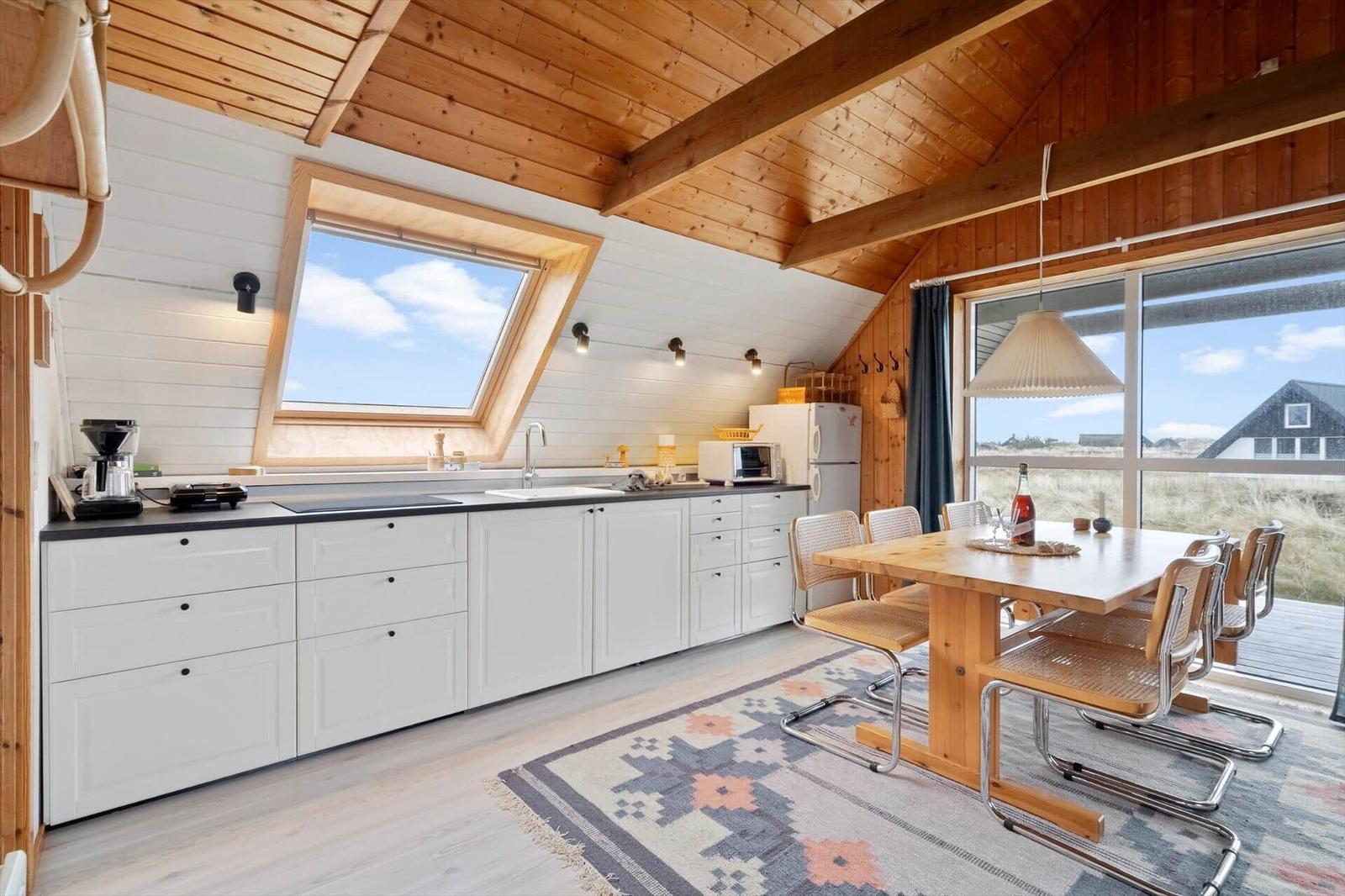 Küche mit Essbereich, Holzdecke und großem Fenster. Tisch mit Stühlen und Teppich.