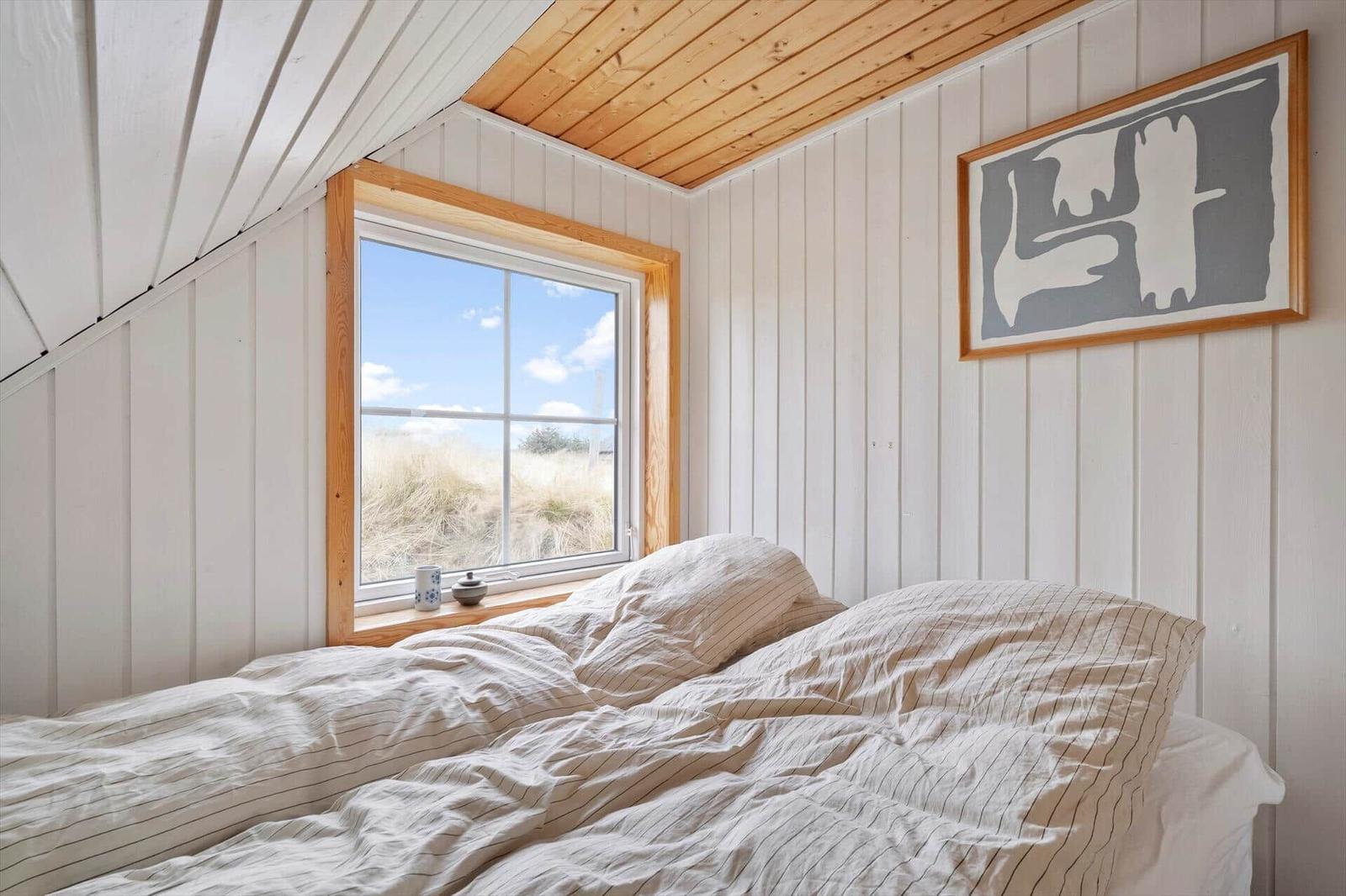 Schlafzimmer mit Fenster und Bett unter Holzdecke.