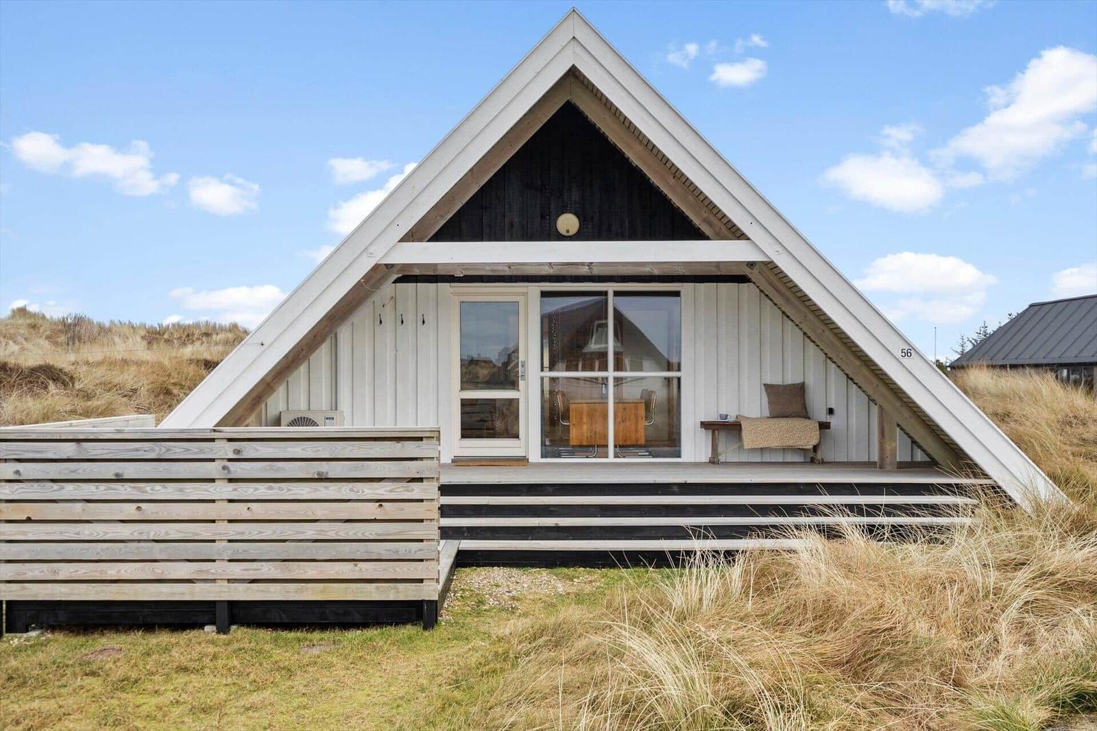 A-frame-Haus mit Holzveranda und Glasfront. Umgeben von Gras und blauem Himmel.