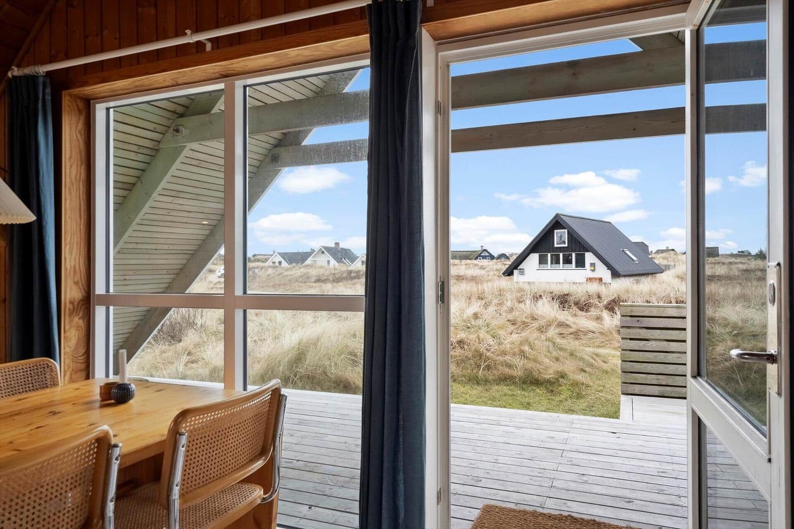 Durch große Fenster Blick auf Dachgaube und Ferienhaus im Grasland.