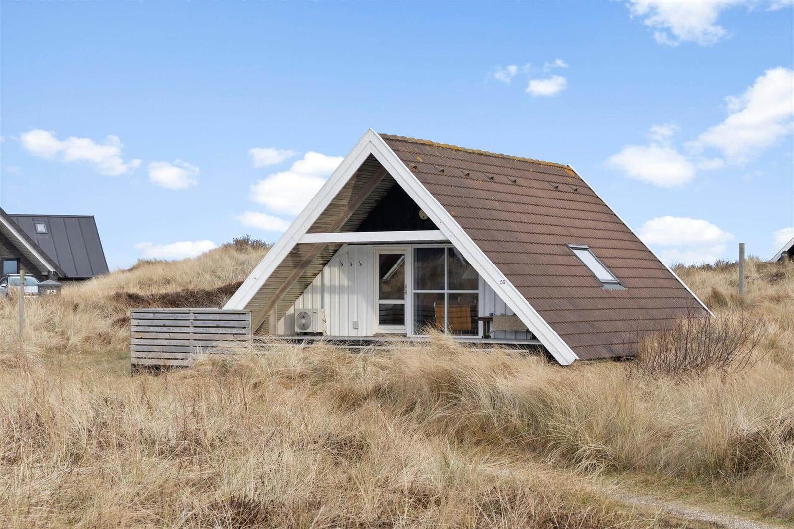 A-frame-Haus mit braunem Dach und Holzverkleidung, umgeben von trockenem Gras unter blauem Himmel.
