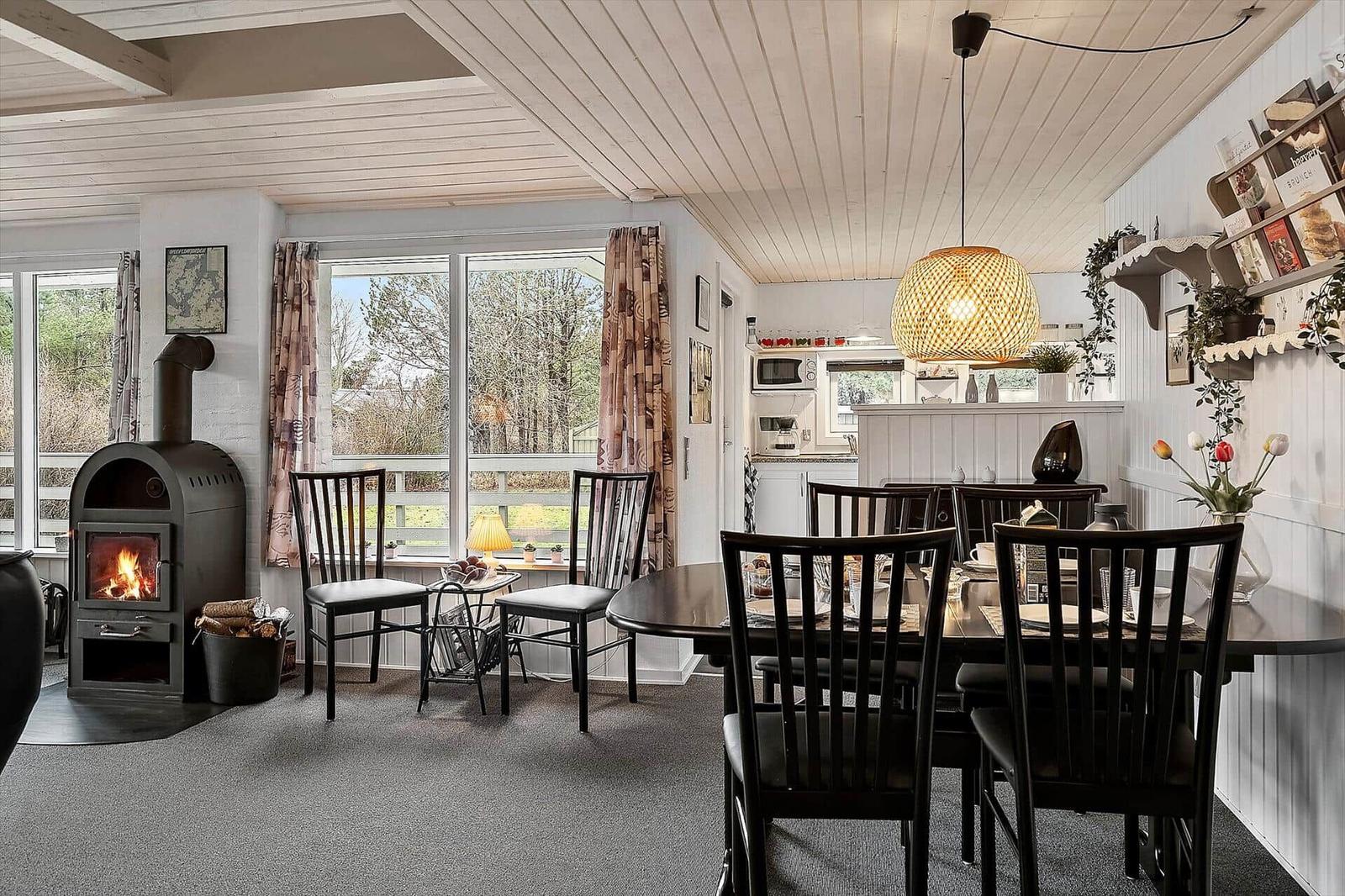 Dining room with table, chairs, and wood stove. Kitchen in background.