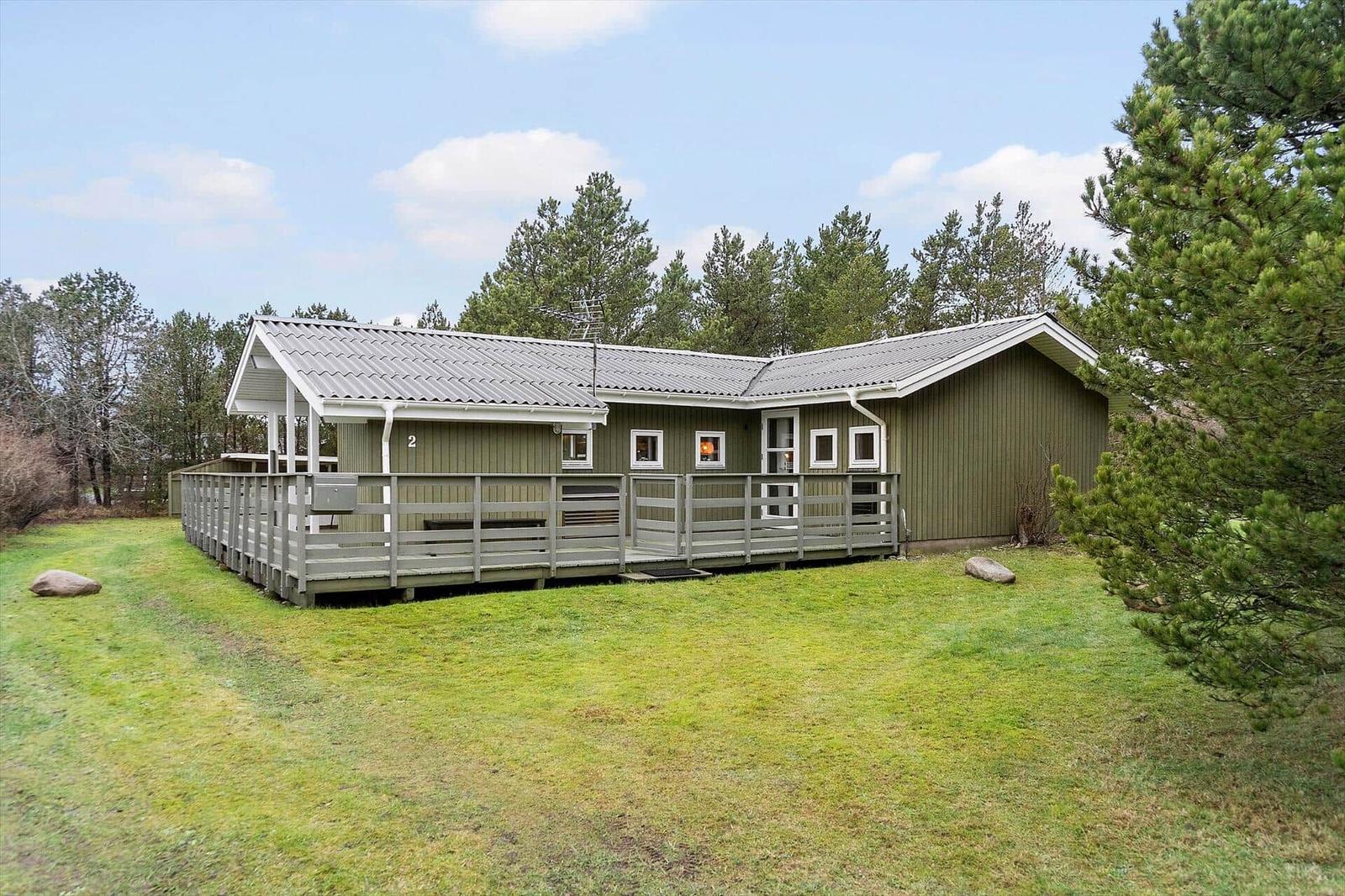 Green holiday home with wooden terrace and view of forest.
