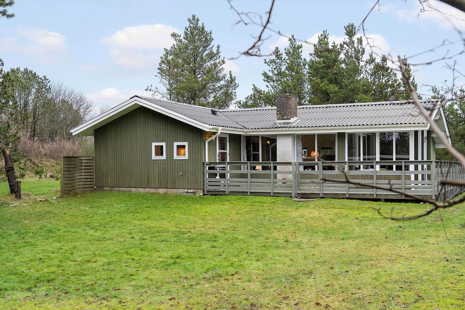 A green house with a porch and large windows stands on a green lawn.