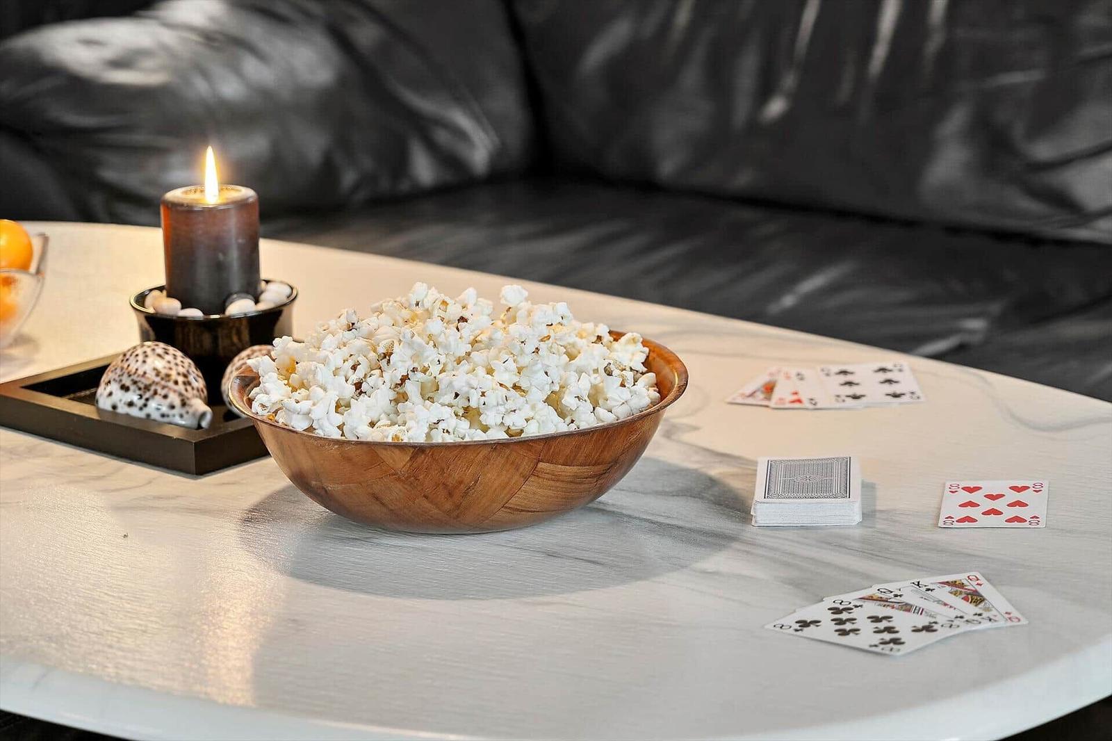 Table with popcorn bowl, playing cards, and lit candle in front of a sofa.