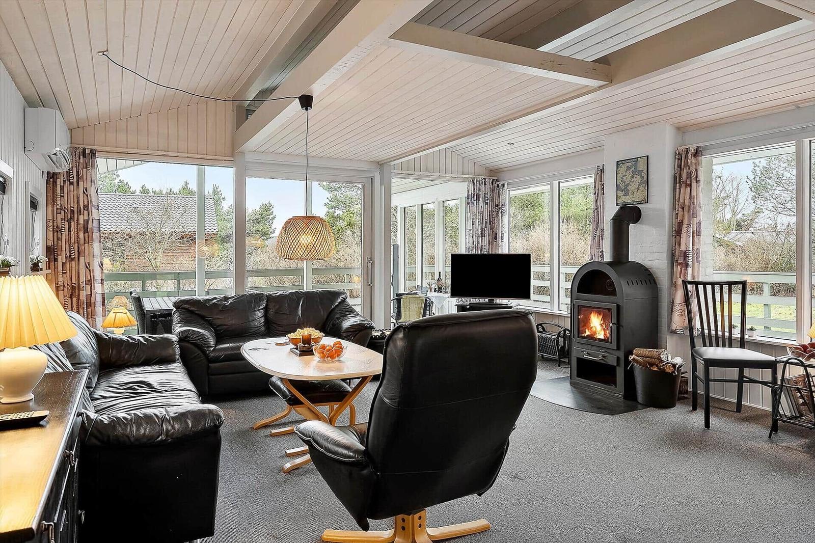 Living room with fireplace, sofa and armchair. Large windows with view of outdoor area.