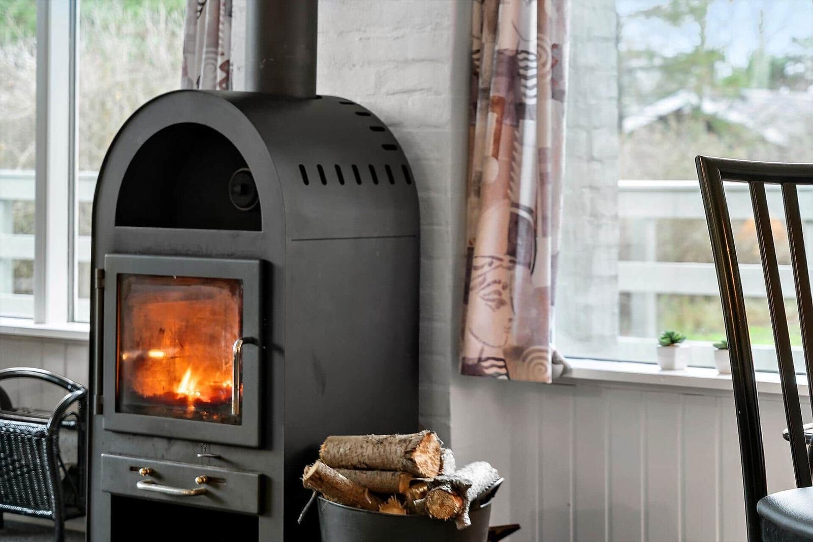 Wood stove with burning fire, firewood, and windows with curtains.