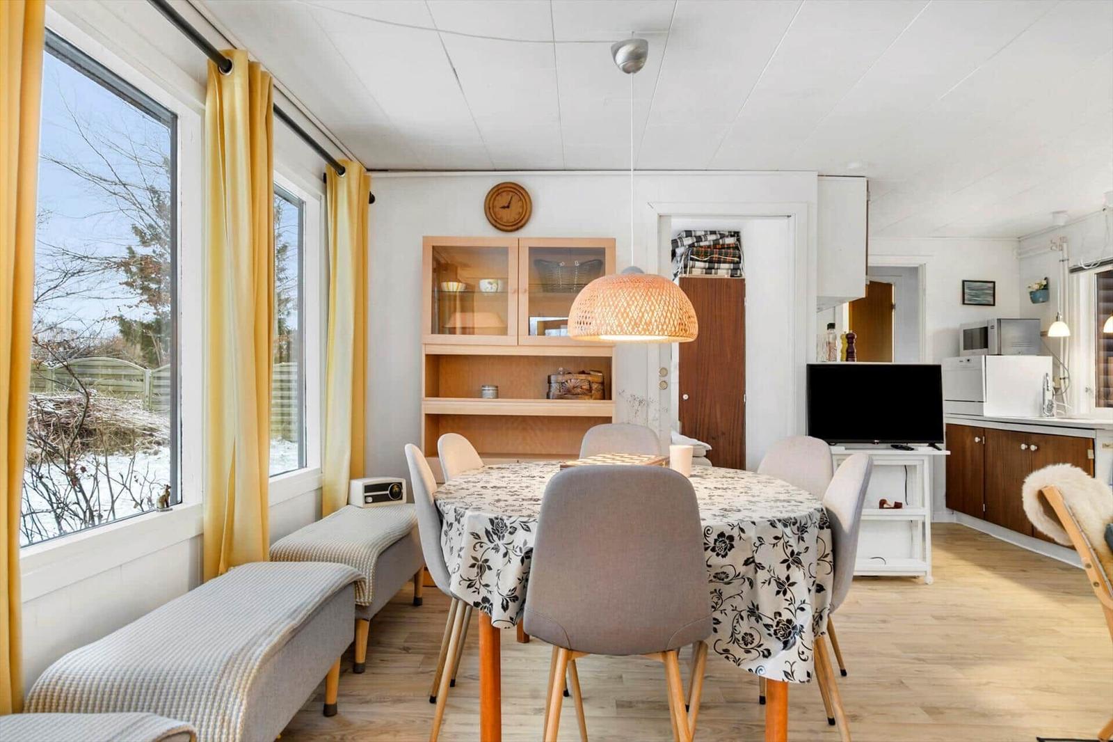 Esszimmer mit runden Tisch, Stühlen und Fenstern mit gelben Vorhängen.