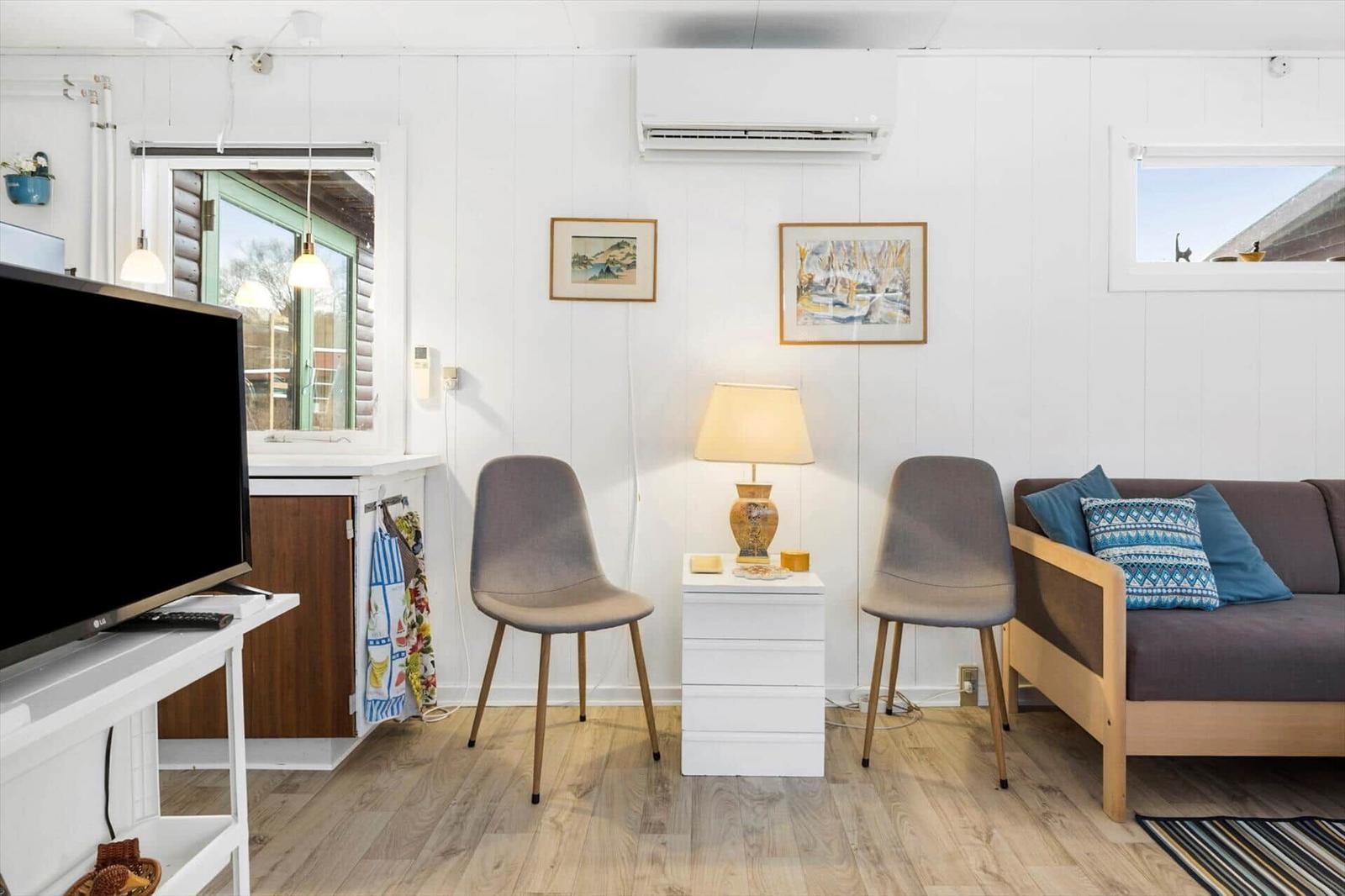 Wohnzimmer mit Sofa, zwei Stühlen, Fernseher und Holzboden.