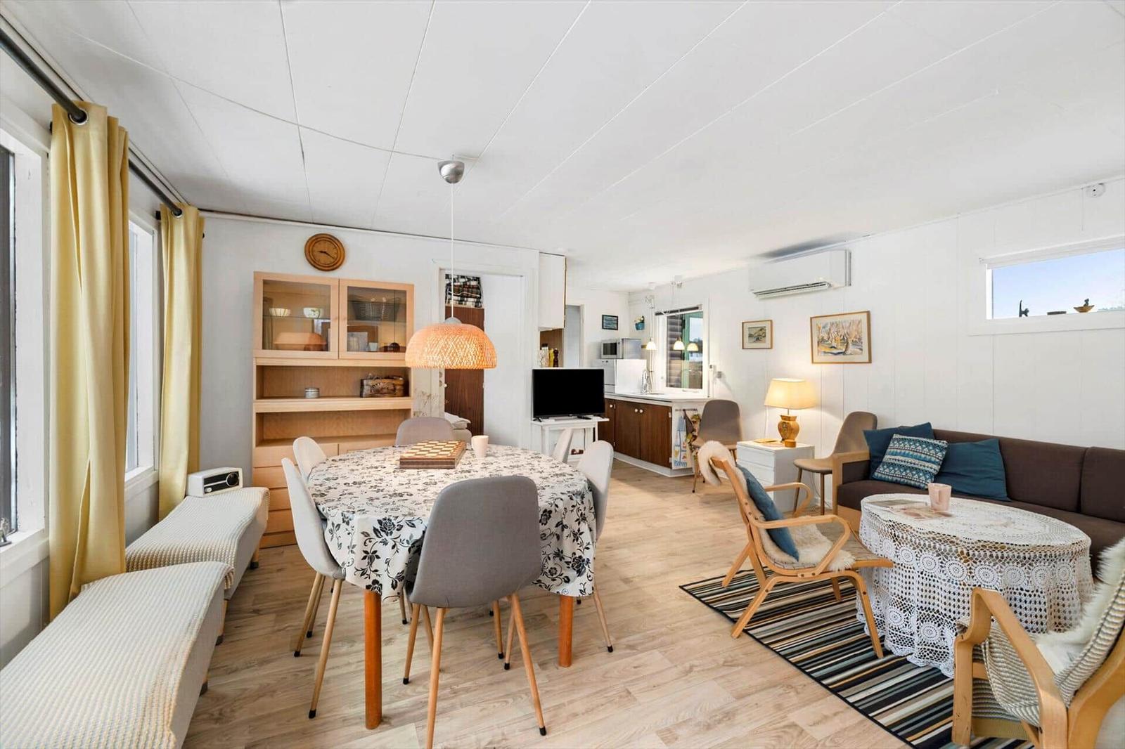 Wohnzimmer mit Esstisch, Sofa und Küchenbereich. Holzboden und weiße Wände.