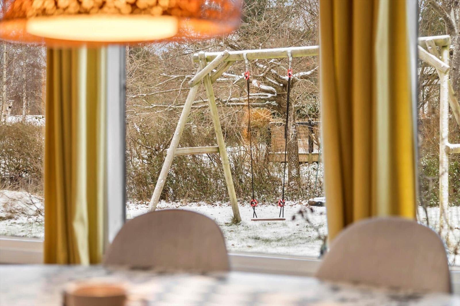 Durch das Fenster ist ein Schaukeltisch im Schnee zu sehen.