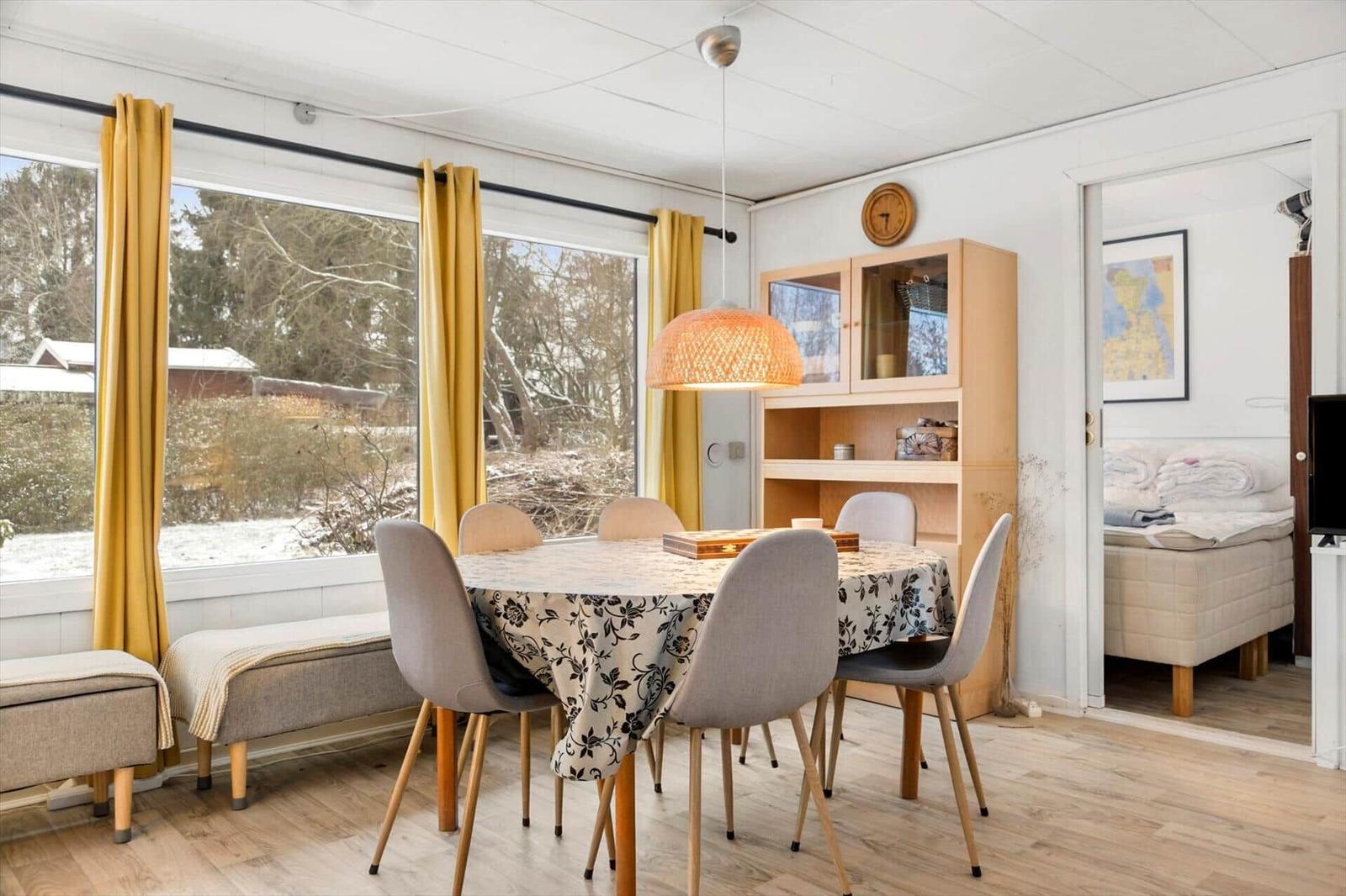 Essbereich mit Tisch, Stühlen und Blick auf Garten. Schlafzimmer im Hintergrund.