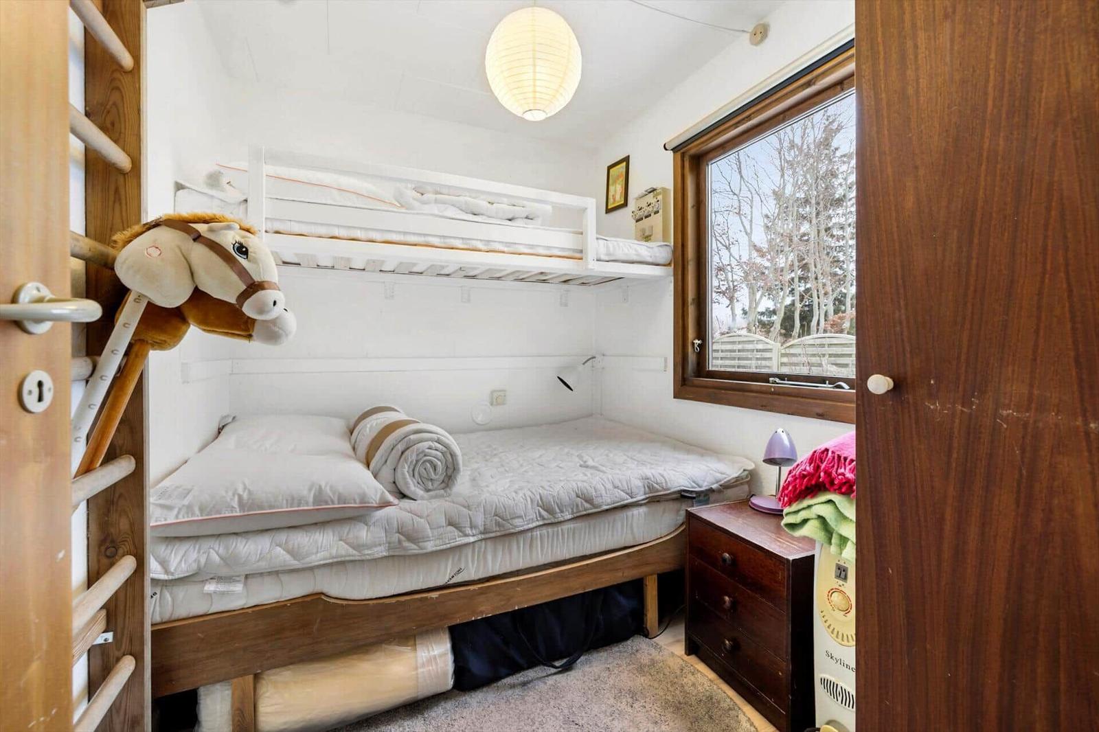 Zimmer mit Doppelbett und Hochbett, Fensterblick auf Bäume.
