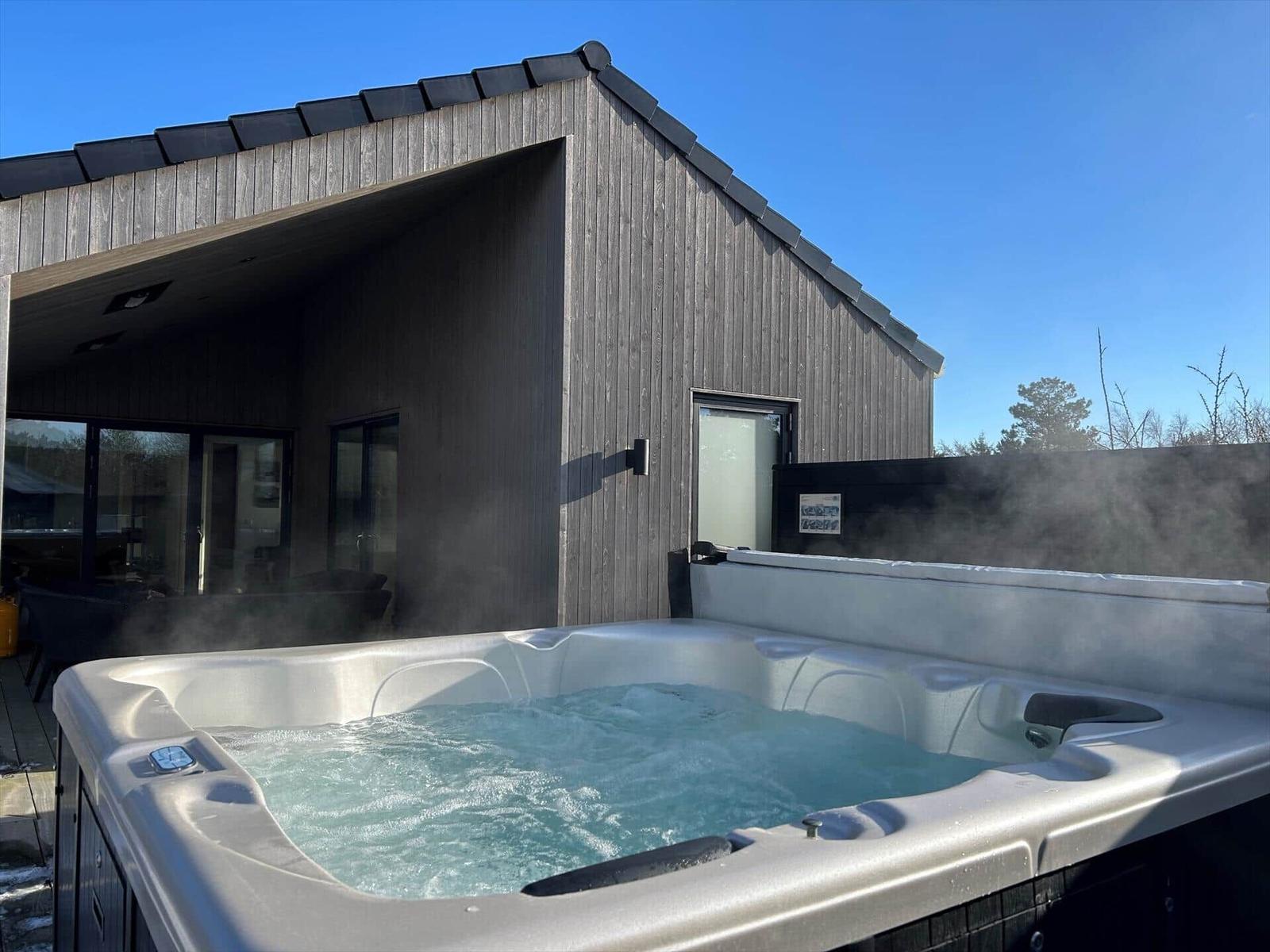 Steamy hot tub in front of a wooden house with large window area.