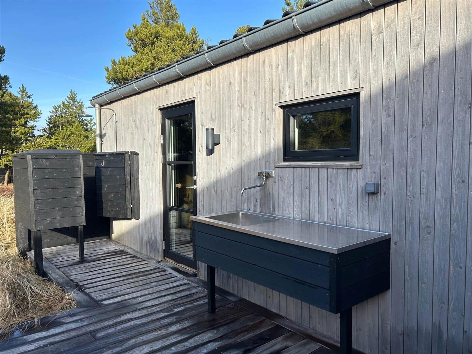 Outdoor area with sink, shower, and wooden terrace beside a house.