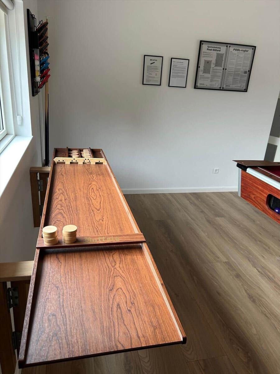 Long wooden table with game pieces and wall rack in room with wooden floor.
