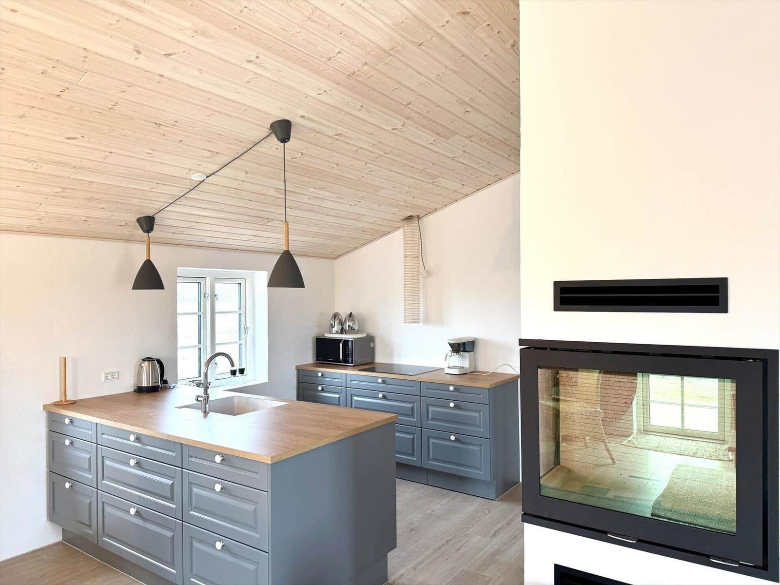 Küche mit Holzdecke, grauen Schränken und Kaminofen.