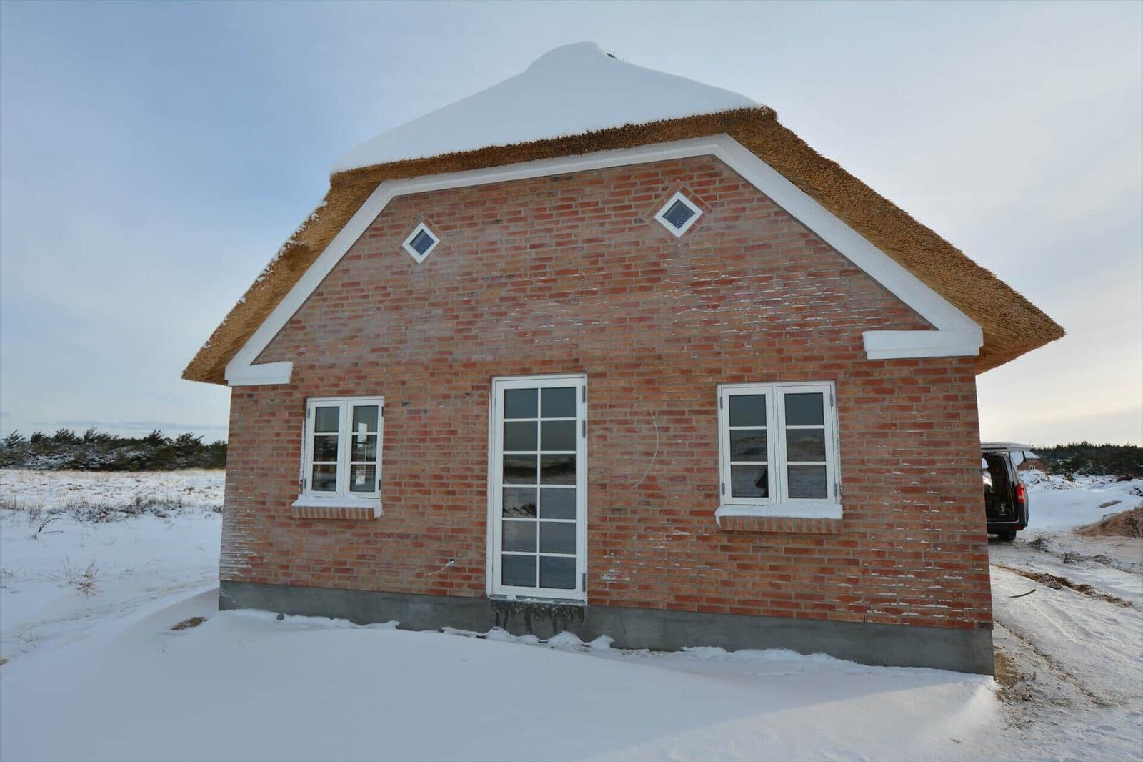 Rotes Backsteinhaus mit strohgedecktem Dach und weißen Fenstern im Schnee.