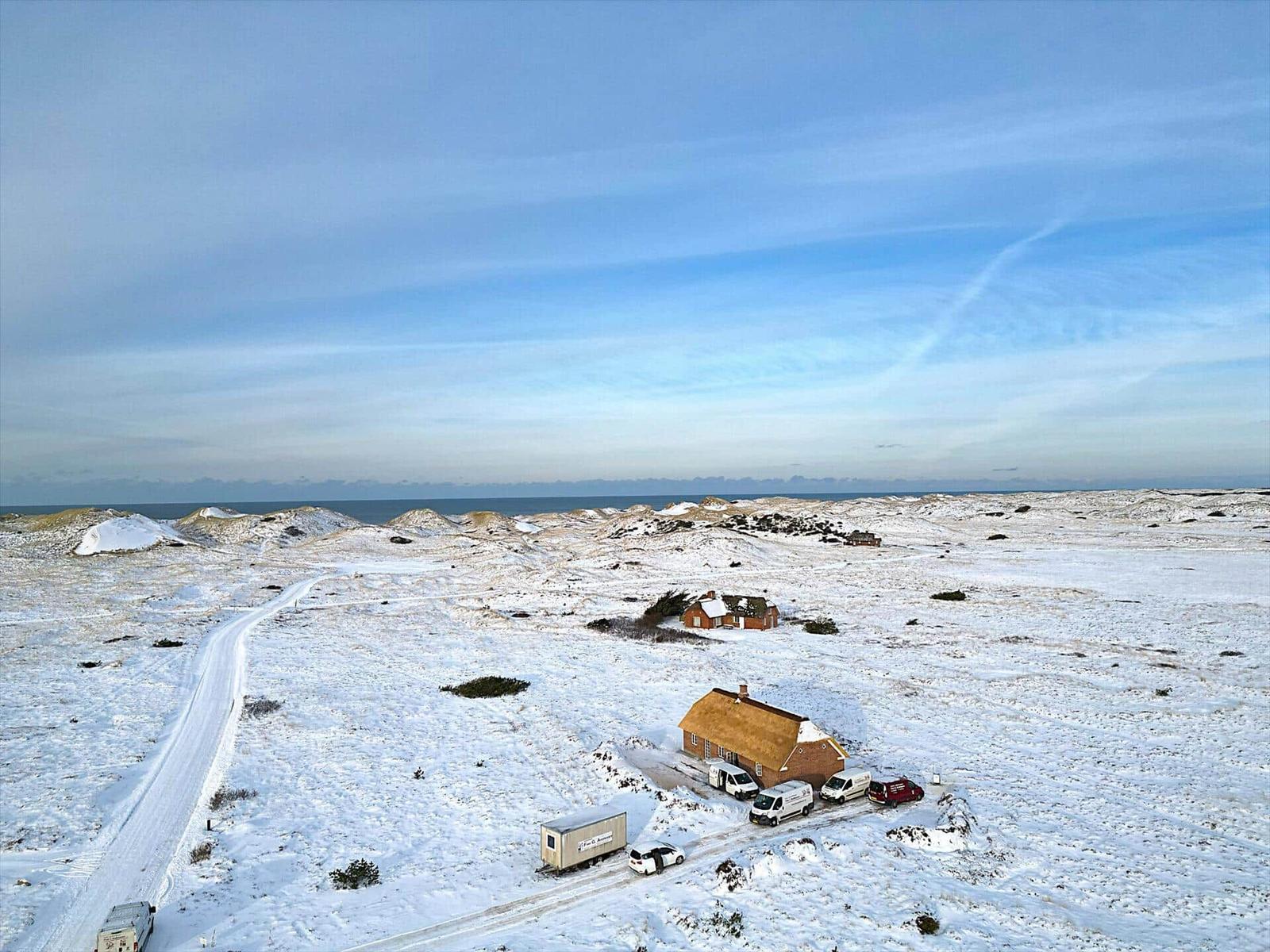 Schneebedecktes Gelände mit Häusern und Fahrzeugen nahe dem Meer.