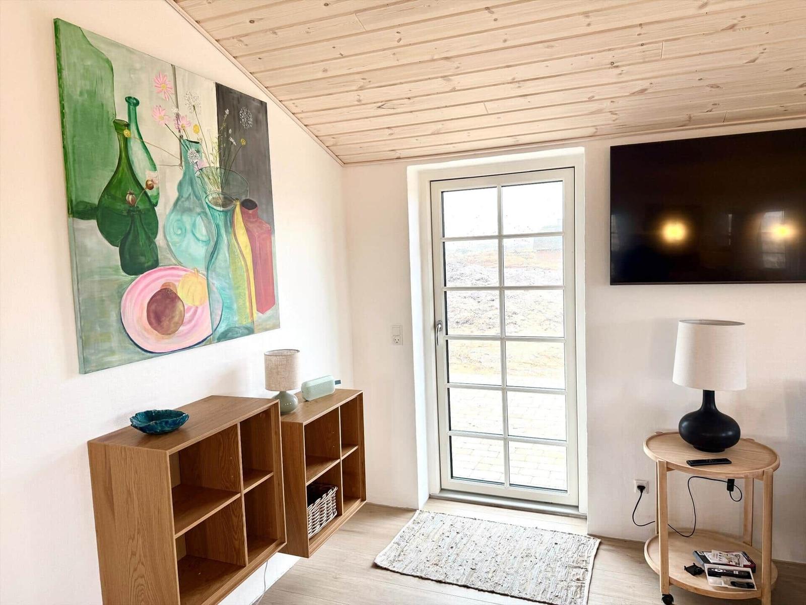 Raum mit Holzdecke, Fernseher, Tür und Wandbild.