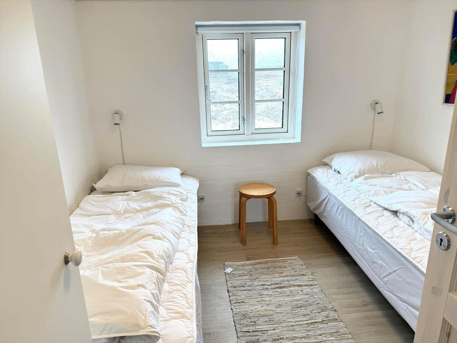 Zwei Einzelbetten, ein Fenster, ein Holzstuhl und ein Teppich.