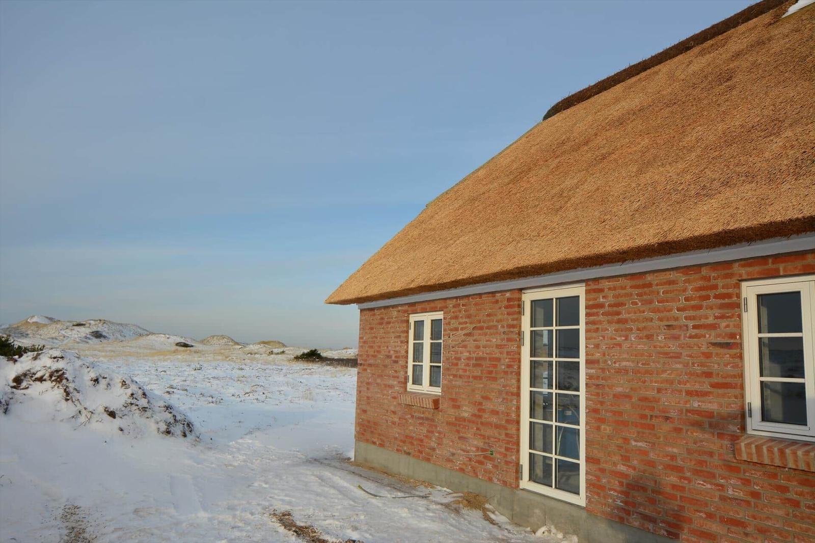 Rotes Backsteinhaus mit Strohdach und weißen Fenstern in schneebedecktem Landschaft.