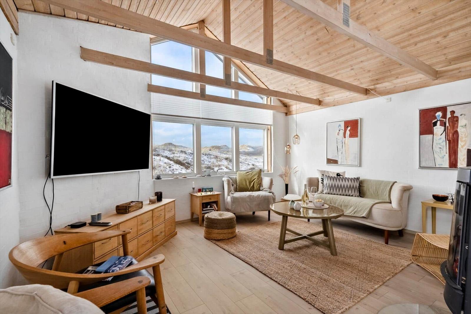 Wohnzimmer mit Holzboden, TV, Sofa und Blick auf verschneite Landschaft.
