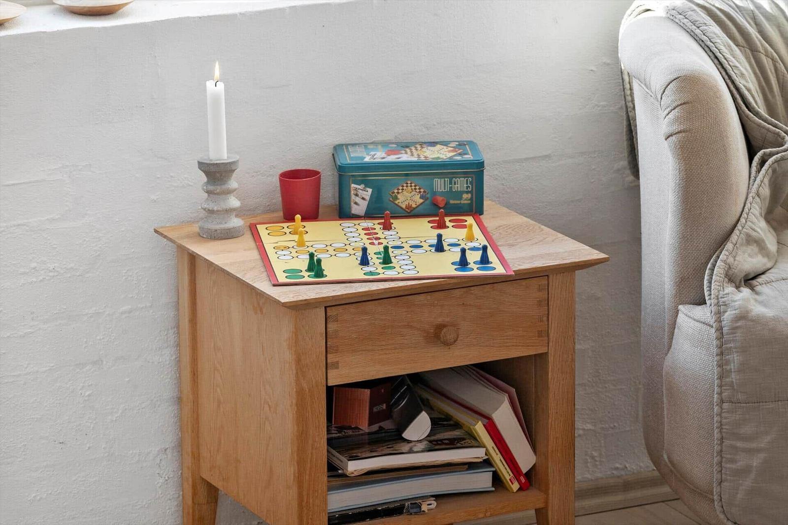 Holzsideboard mit Brettspiel, Kerze und Bücherregal neben Sessel