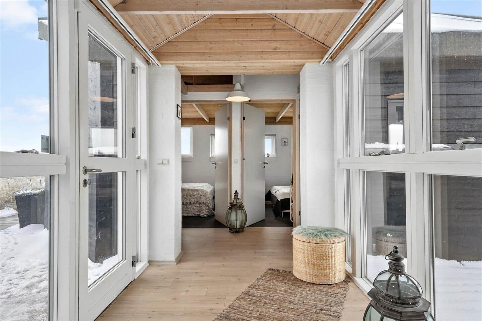 Helle Eingangshalle mit Holzboden und großen Fenstern. Blick in Schlafzimmer mit Betten.