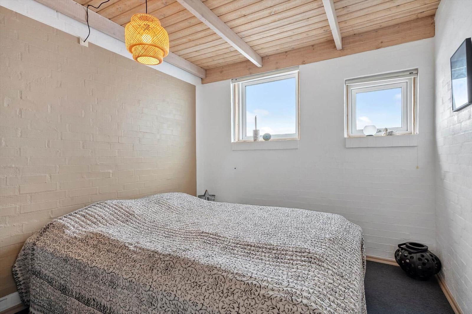 Schlafzimmer mit Bett, zwei Fenstern und Holzdecke.