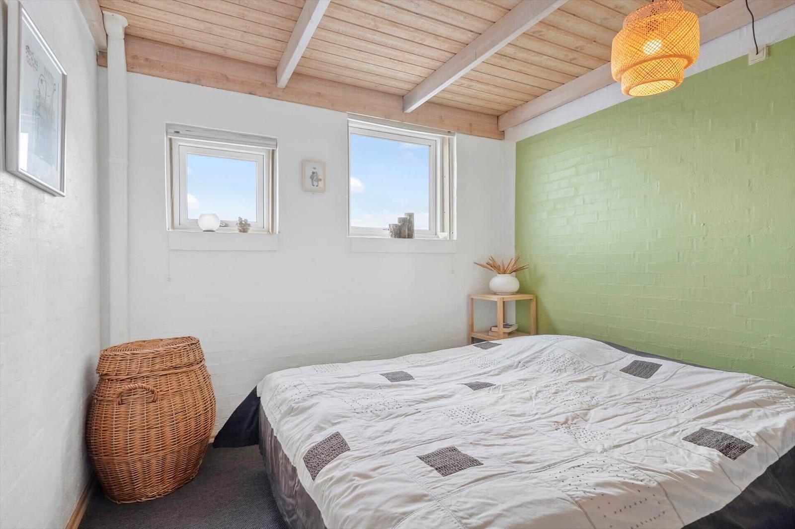 Schlafzimmer mit Bett, zwei Fenstern und grüner Wand.