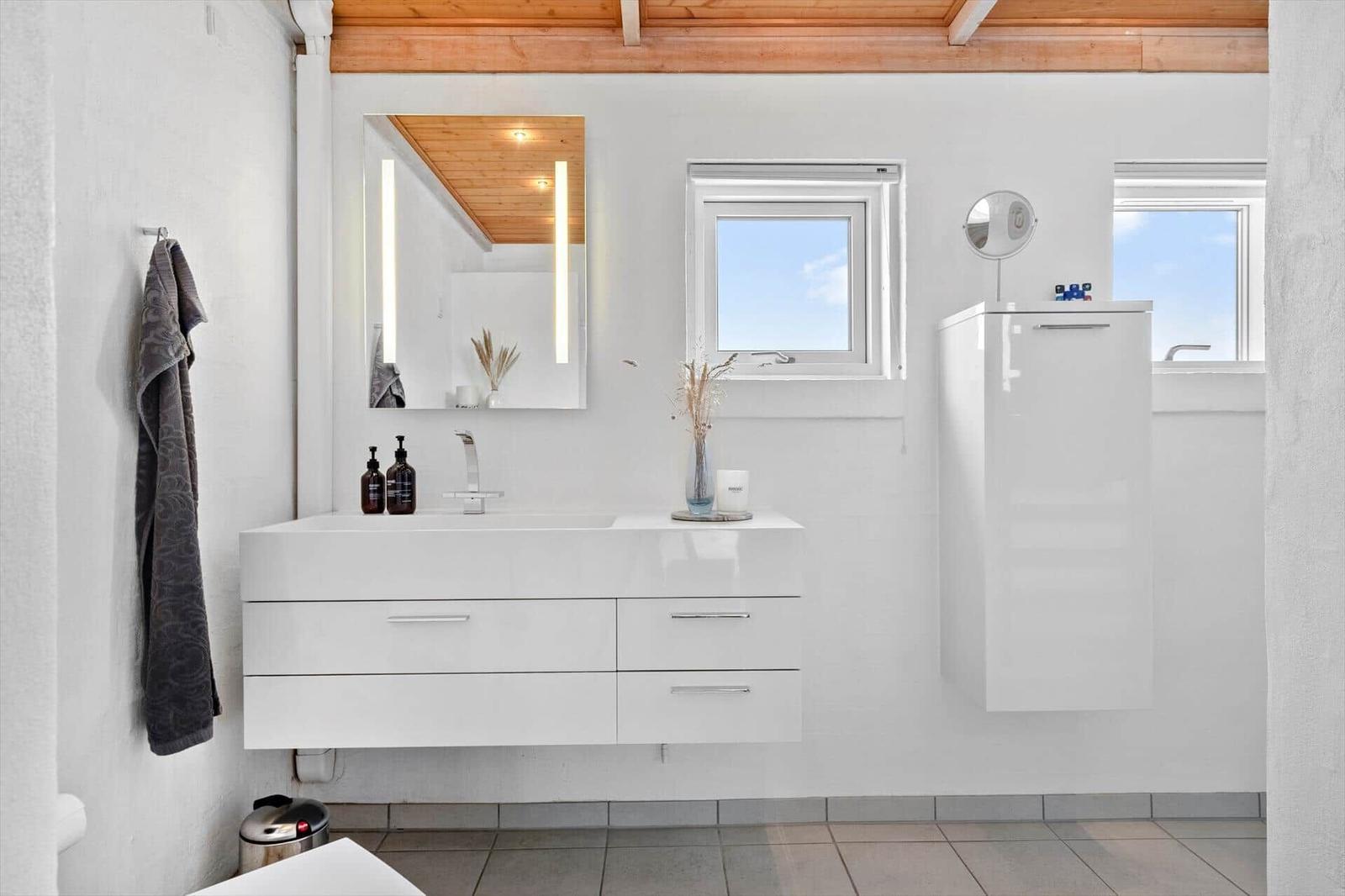 Badezimmer mit weißem Waschbecken, Spiegel und Fenstern.
