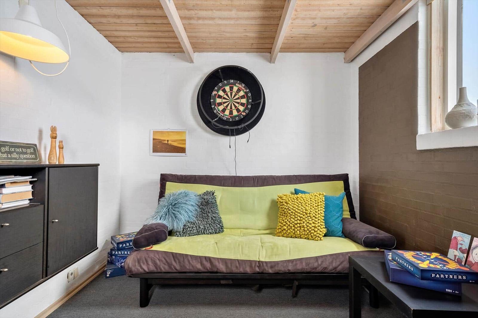 Raum mit Sofa, Dartboard und Bücherregal an der Wand.