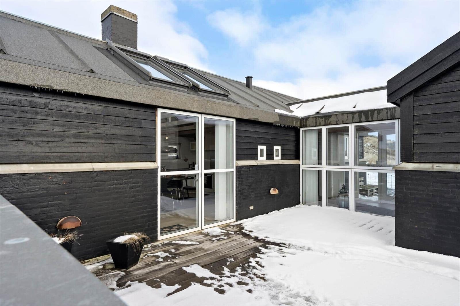 Schwarze Holzwand mit Glasfront und Schneedecke im Hofbereich.